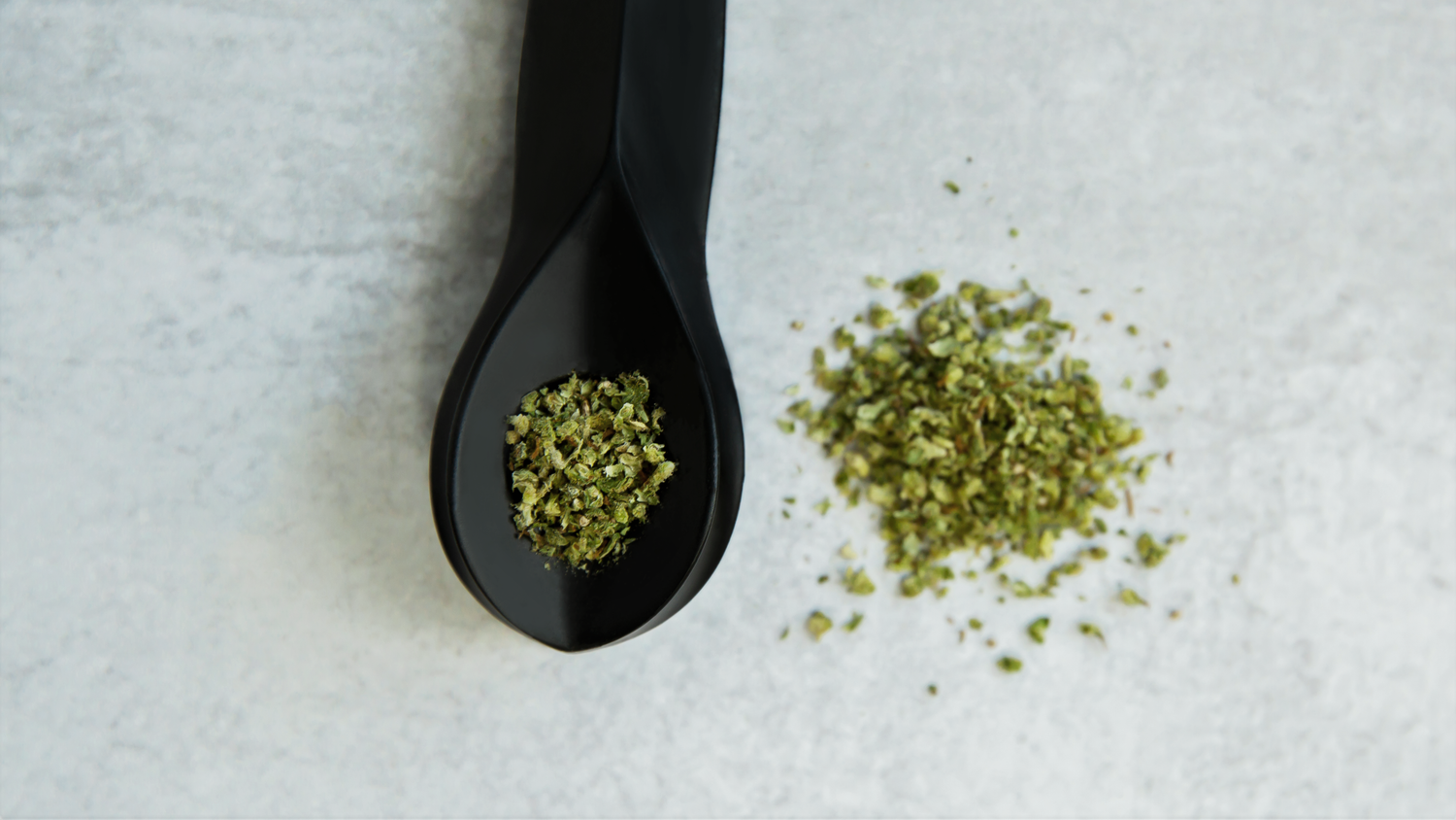 A black KØL pipt is filled to the brim with cannabis. A small pile of cannabis sits beside it on the countertop.