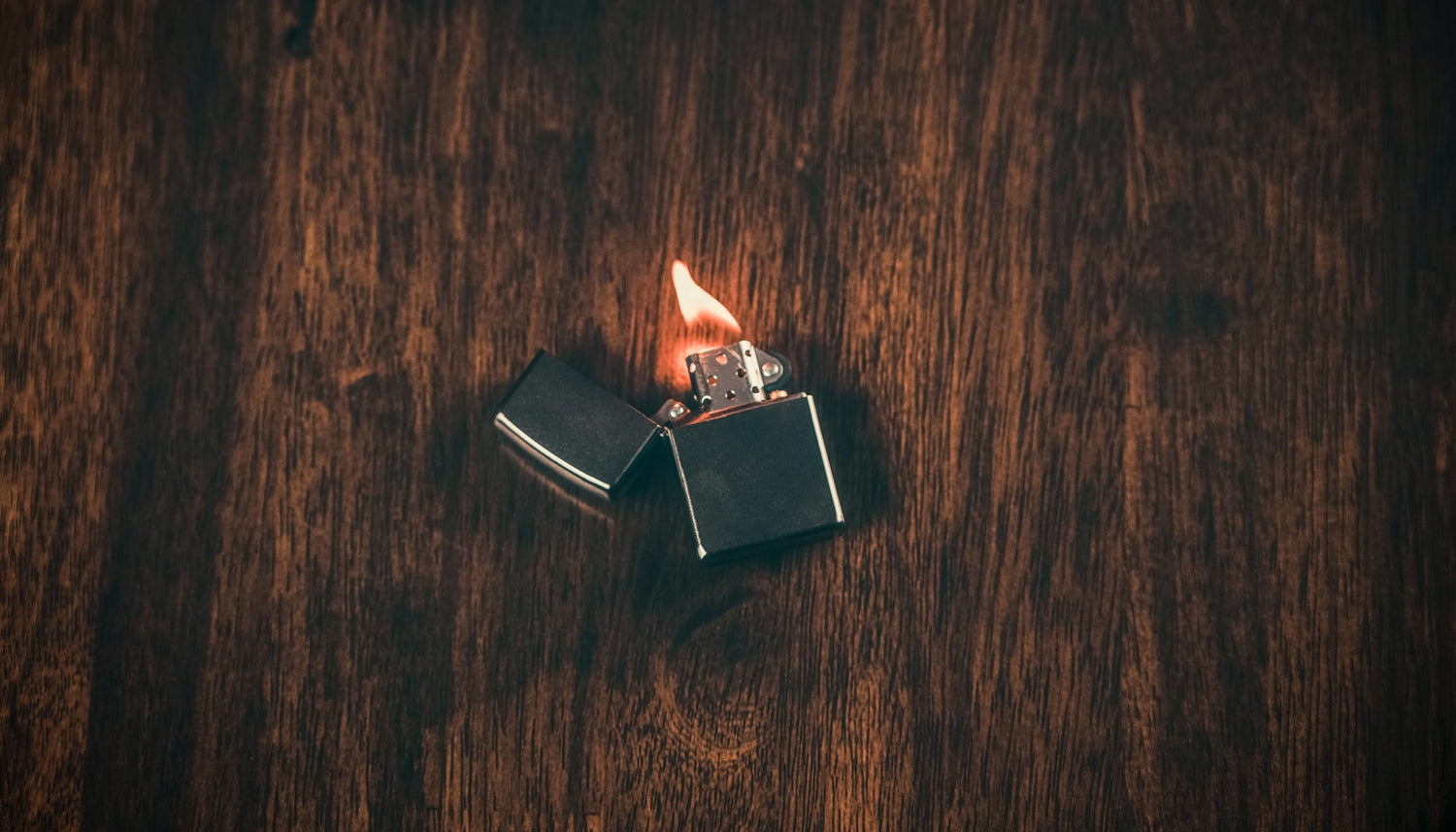 A lit butane lighter is on top of a wooden table.