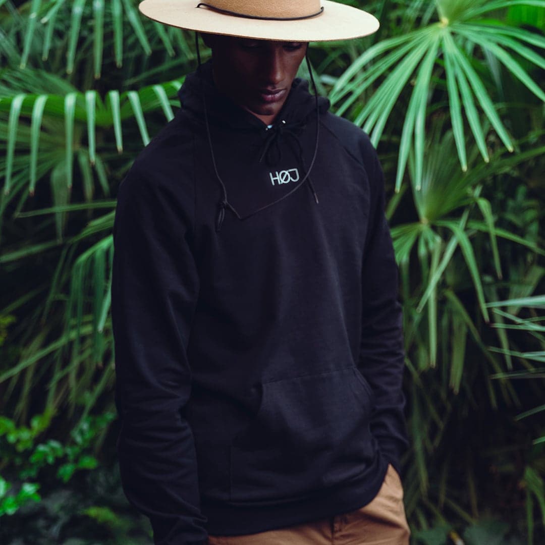 man with black HØJ hoodie on green plant background