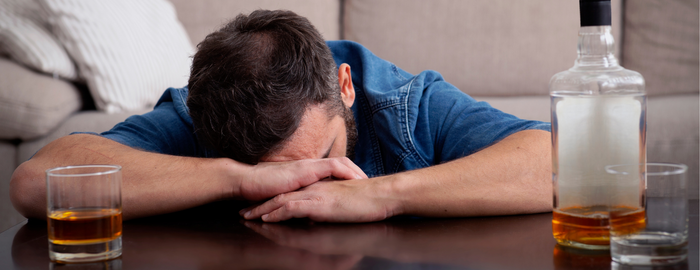 man leaning over a table with alcohol bottle and glasses