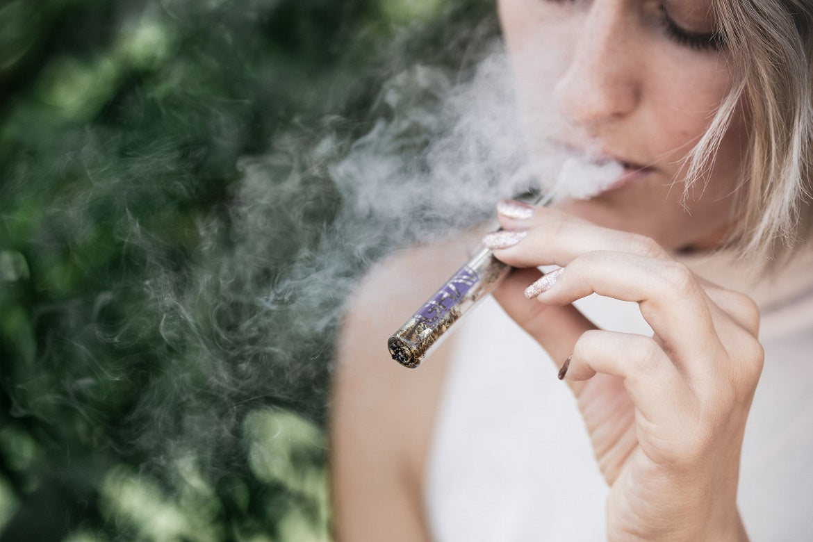 A woman holds a small glass pipe in her left hand.