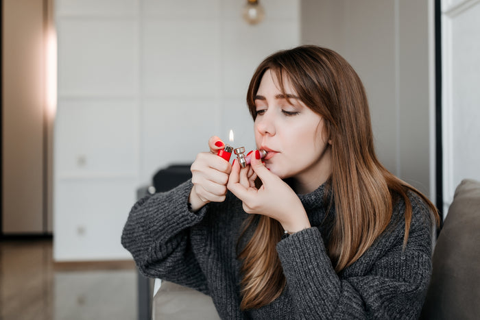 A woman with brown hair smokes out of a weed pipe inside her apartment