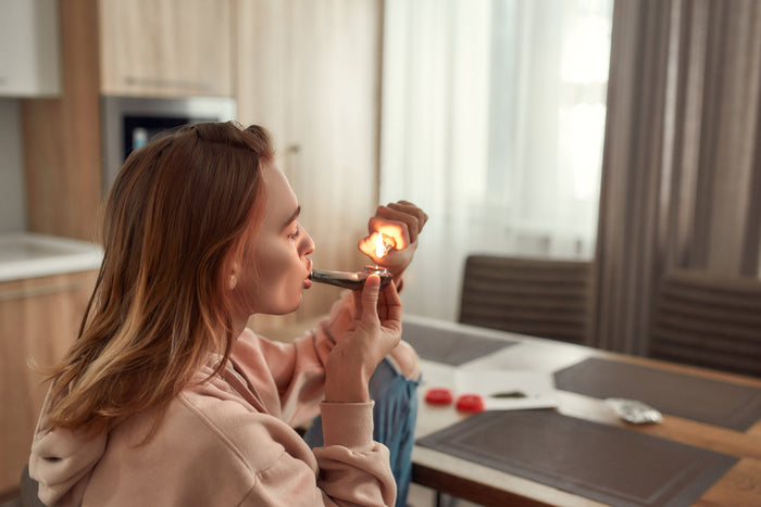 A caucasian woman lights a cannabis pipe