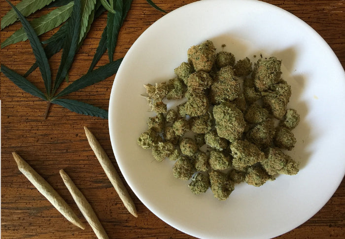 A plate full of cannabis is placed next to three joints and marijuana leaves