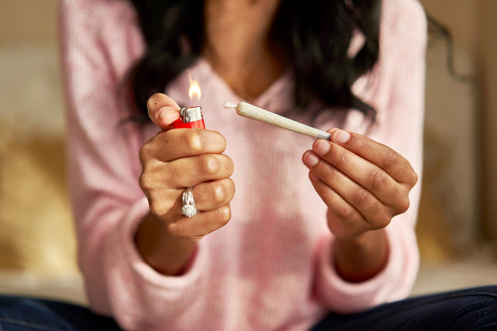 A black woman holds a perfectly rolled joint up to a red lighter