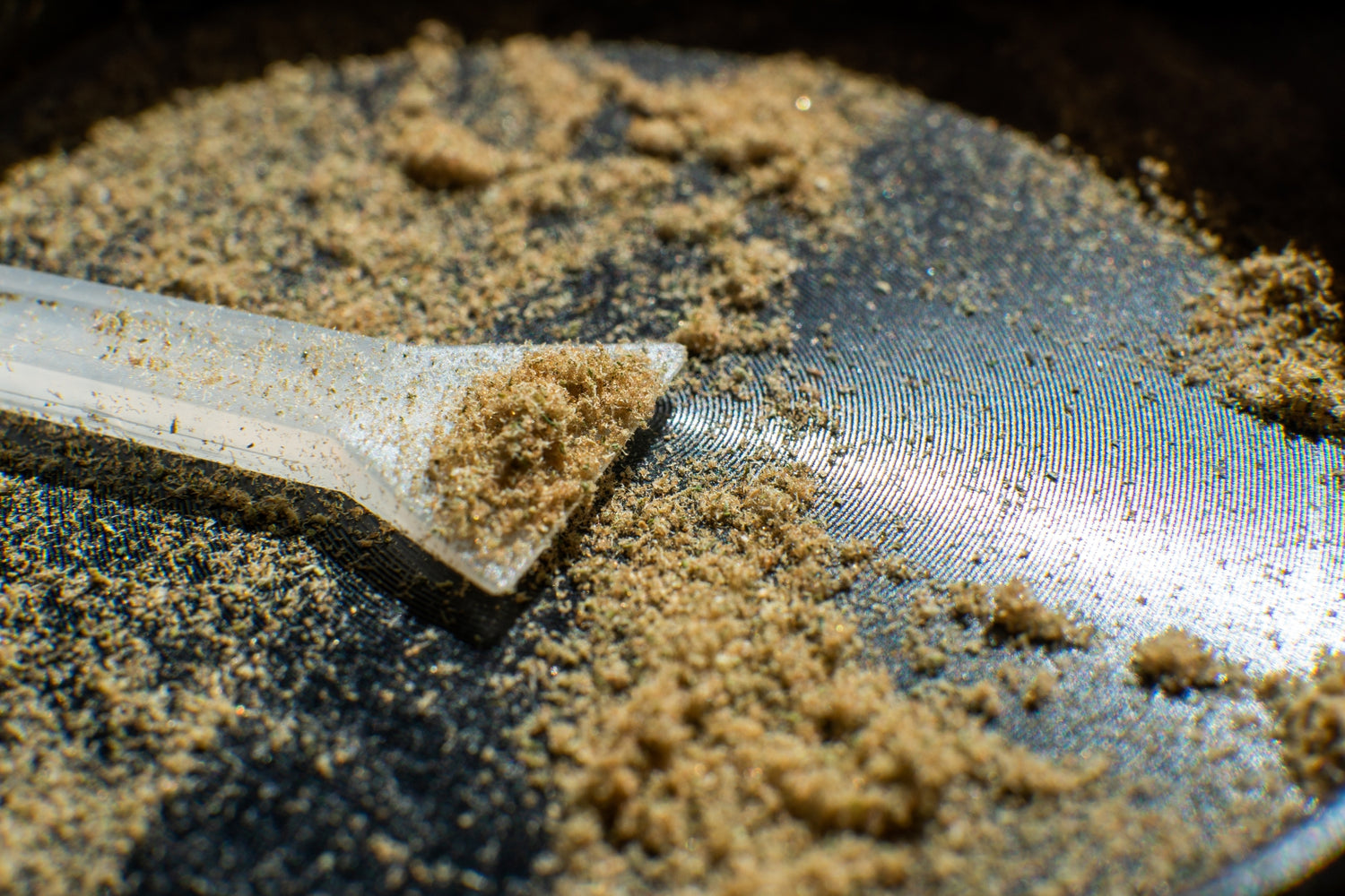 A glittering green pile of kief sits in the bottom of a black grinder
