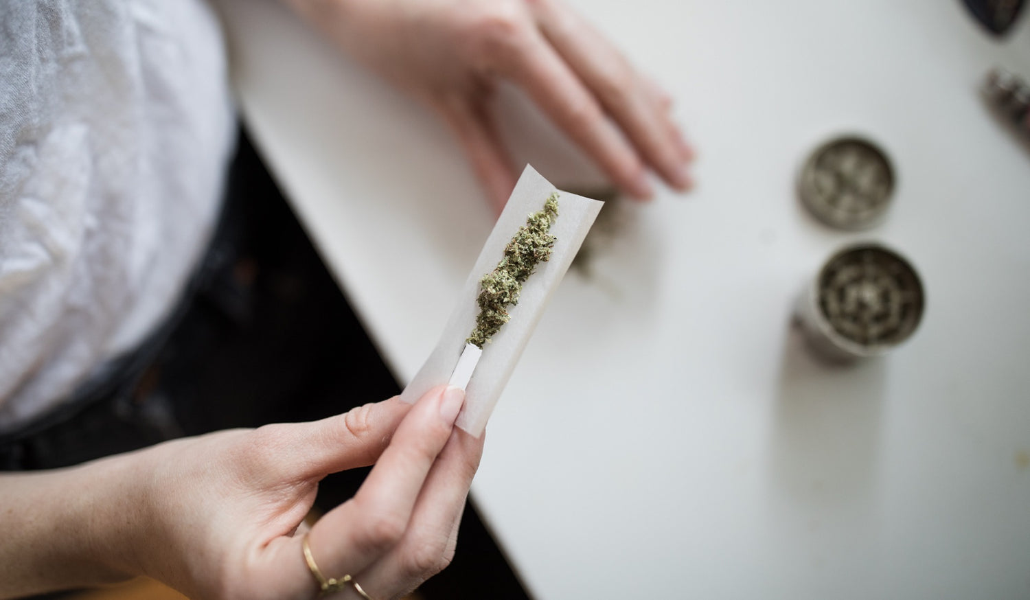 A hand holds a clear rolling paper full of ground cannabis. 