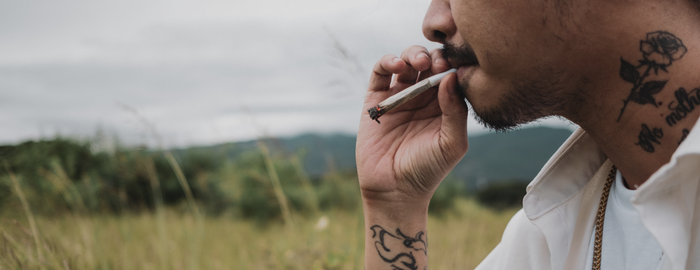 man with tattoos smoking weed outside