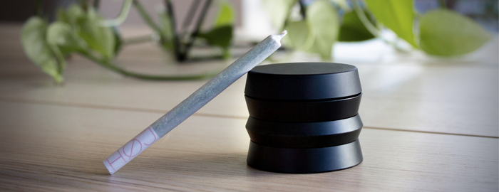 weed joint relying on a black grinder over a wooden table
